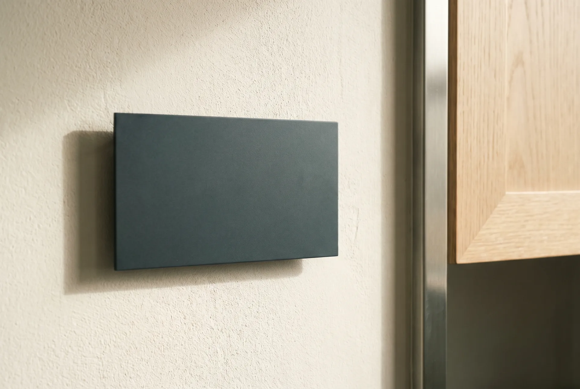A dimensional matte deep-slate metal sign plate floating on concealed standoffs against a linen ivory plaster wall.