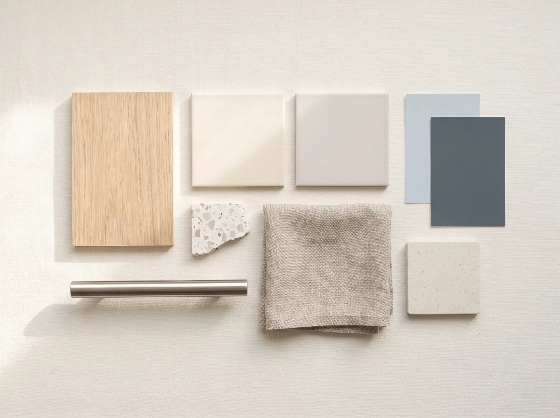 A material board laid out on ivory paper: white oak veneer, porcelain tile squares, a terrazzo chip, brushed nickel, folded linen and paint chips in powder blue and slate.